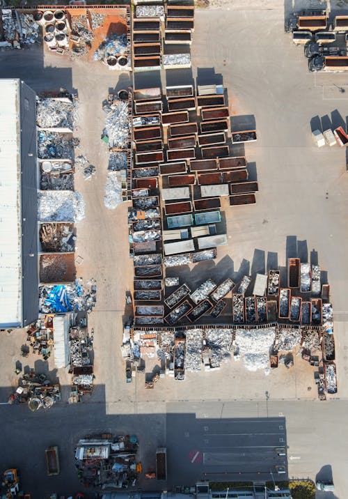 Vue aérienne d’un terrain de recyclage avec de vastes bacs et piles de matériaux triés, près d’un bâtiment, illustrant l’installation d’une machine de tri des déchets.